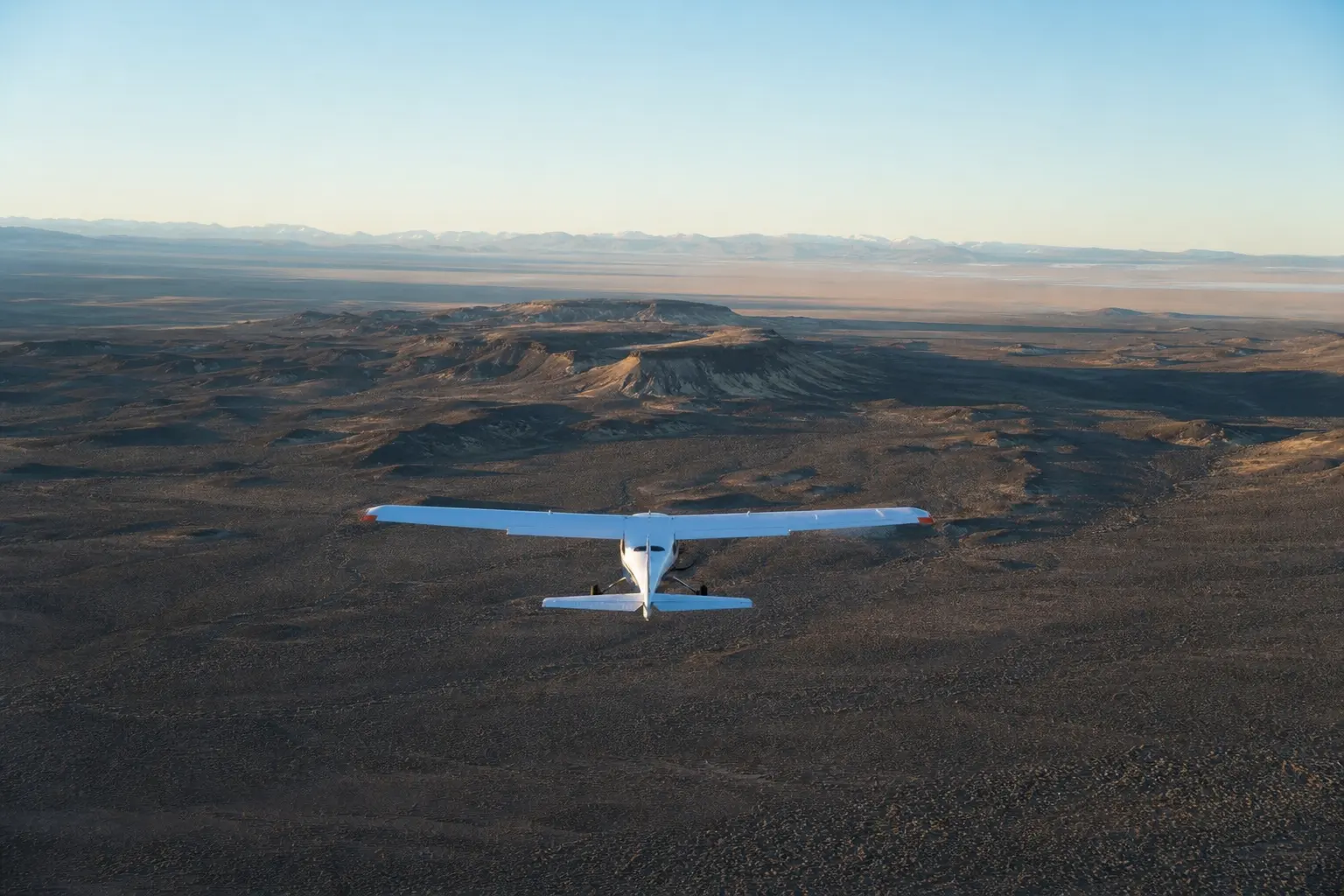 A fixed-wing survey aircraft flying a straight transect over open high-desert terrain at golden hour